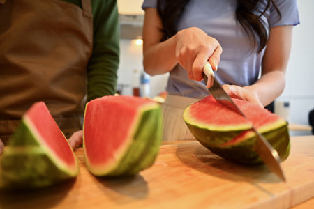 Woman cutting fresh watermelon while standing in kitchen at home. Healthy breakfast, weight loss...