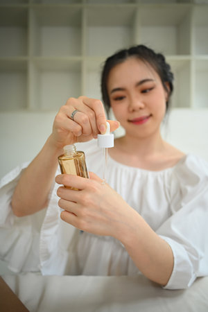 Female beauty blogger dropping facial essential serum on her hand and recommending quality of skincare.の写真素材