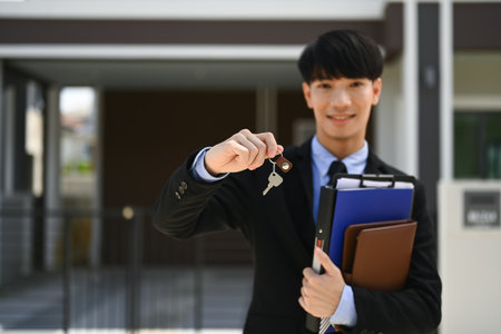 Realtor hands holding keys standing in front of new house. Real estate mortgage and property investment concept.の写真素材