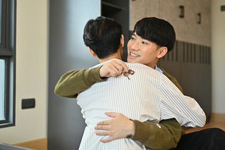 Happy gay man couple celebrating moving into new home and hugging each other. LGBTQ, relocation and real estate property.の写真素材