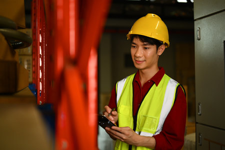 Handsome male worker checking stock and order details while standing near shelves full of packed boxes.の写真素材