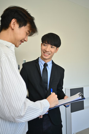 Happy young asian man signing contract with realtor. First property purchase, ownership and real estate concept.の写真素材