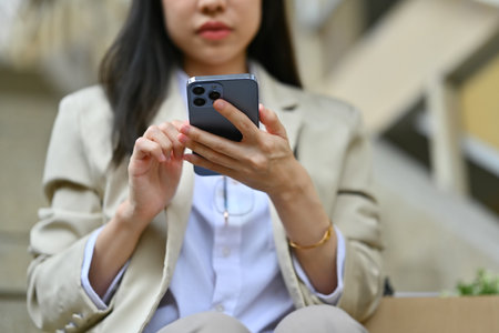 Businesswoman sitting on stairs outside office building and texting messages, chatting in social on smartphone.の写真素材