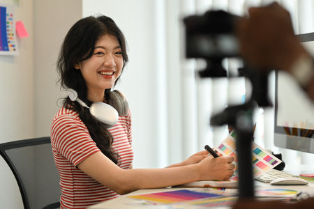 Cheerful female freelancer working on new design project and recording vlog on digital camera.