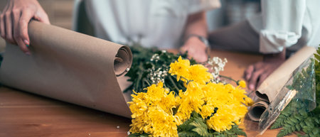 Female florist in apron is arranging, wrapping bouquet of white roses on a wooden table in craft paper.の写真素材