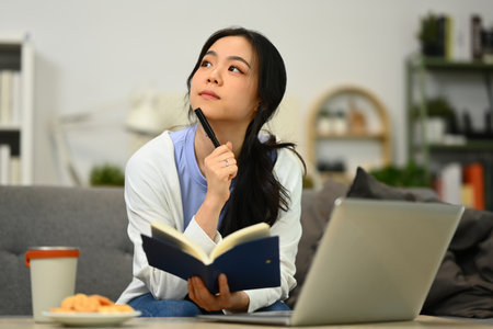 Thoughtful young female freelancer thinking, solving problem and using laptop in living room.