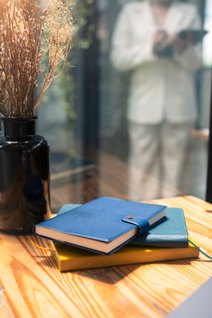 Books and dried flower in vase beside window with sun light. Comfortable workplace.