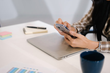 Woman texting message and checking social media on smartphone while sitting at her workplace.