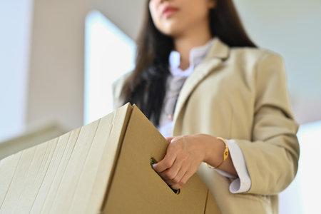 Fired Asian female worker holding cardboard box with belongings walking out of the office building. Unemployment concept.の写真素材