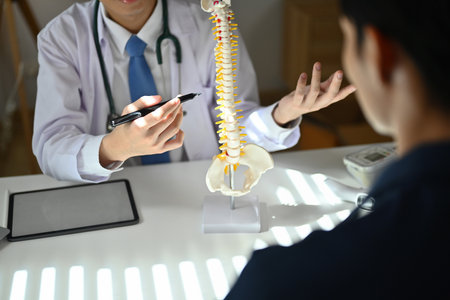 Experienced male orthopedist giving consultation about scoliosis or spinal problems during medical...
