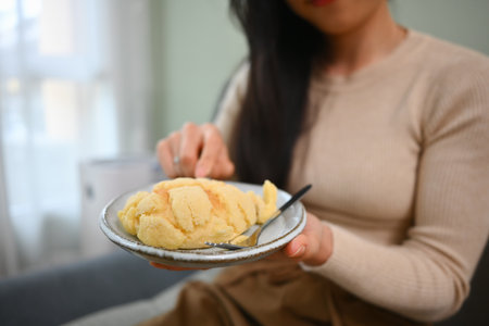 Cropped shot of young asian woman wearing casual clothes holding plate of sweet bun with sugar on top.の写真素材