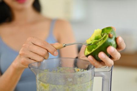 Closeup woman putting avocado into blender to making healthy smoothie. Dieting and healthy lifestyle...