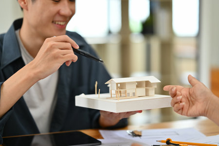 Cropped shot of architect man with house model explaining housing project idea to client.