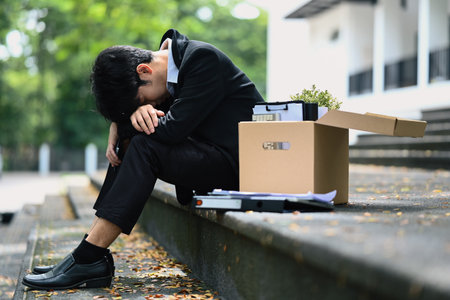 Sad, upset businessman sitting hopelessly on stairs of building with box of personal stuff. Unemployed concept.の写真素材