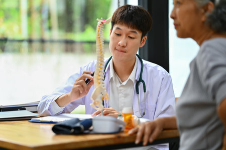 Orthopedist giving consultation about scoliosis or spinal problems to mature female patient during medical exam.の写真素材
