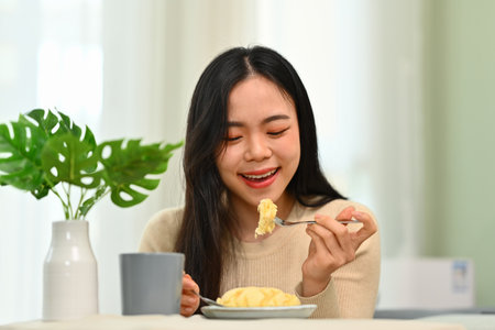 Happy young asian woman in casual clothes having breakfast at home. Concept of wellness, food and domestic lifestyle.の写真素材