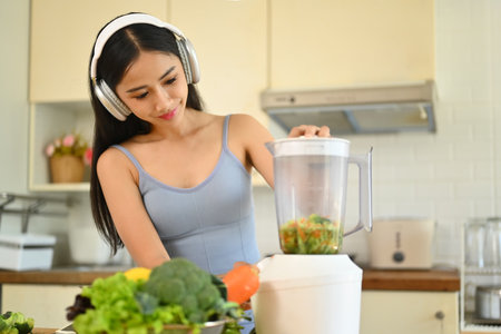Charming young woman in headphone making healthy smoothie in kitchen. Healthy lifestyle concept.の写真素材