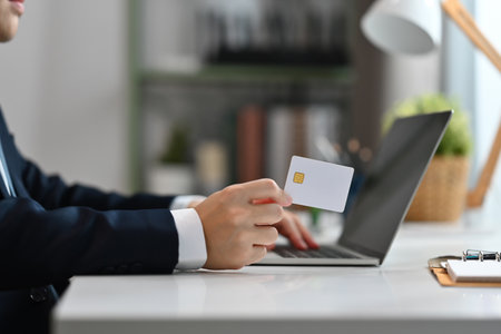 Cropped shot businessman holding plastic card paying with credit card online on laptop. E-commerce, internet banking concept.の写真素材