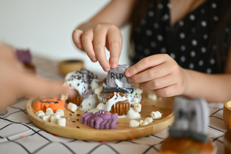 Cropped shot of little girl decorating Halloween cupcakes, preparing for holiday party in kitchen.の写真素材