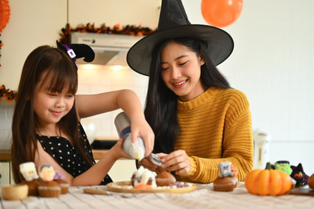 Happy mother with little daughter preparing delicious sweet dishes for Halloween party in kitchen.の写真素材