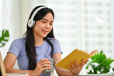 Young woman in headphone reading book, enjoying leisure weekend time at home.の写真素材