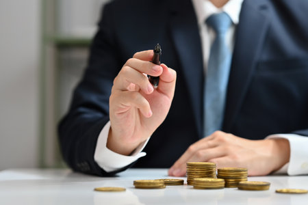 Businessman holding a pen and pointing something with stack of gold coin. Investment and financial management concept.の写真素材
