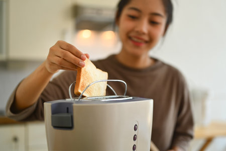 Close up of young woman toasting bread with toaster in the morning for breakfast.