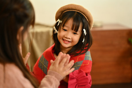 Cute little girl sitting on the floor in living room with friend playing clapping patty cake game on hands, enjoying leisure time together.の写真素材