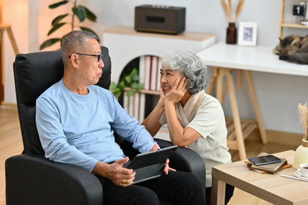 Modern senior couple enjoying talking and using digital tablet together at home.の写真素材