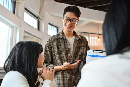 Friendly asian man holding clipboard presenting idea, explaining plan, task to colleagues at...