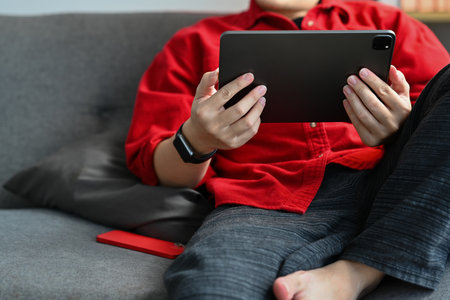 Relaxed young man sitting on couch and browsing internet or watching social media videos on digital...