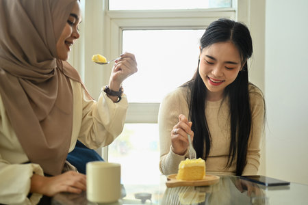 Happy young women friends eating cake and spending leisure time together in coffee shop.