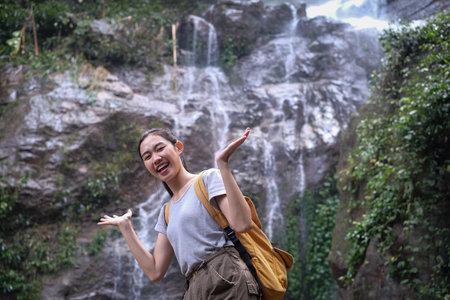 Overjoyed female traveler with backpack raising arms relaxing at tropical nature waterfall.の写真素材