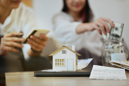 A house model and bills on table with couple planning to buy their future new house on background.の写真素材