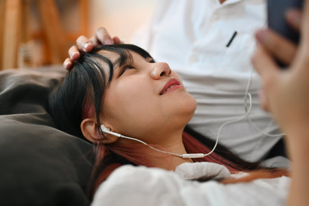 Pleasant young woman using mobile phone and listening music new playlist on couch with her boyfriend.の写真素材