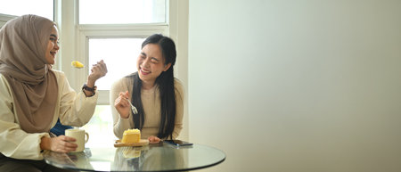 Two cheerful women friends having great time while eating cake in cafe, copy space for your text.の写真素材