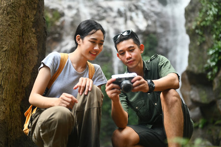 Happy young couple resting in front of a waterfall and checking pictures on camera.の写真素材