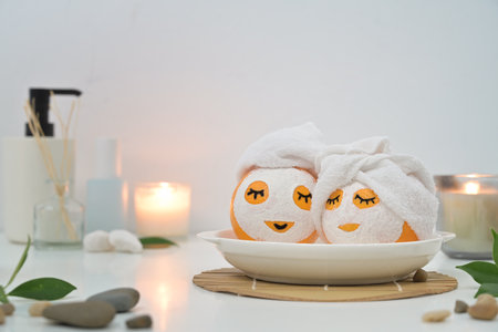 Oranges in face masks and towels surrounded by candles on white background. Spa treatment concept.の写真素材