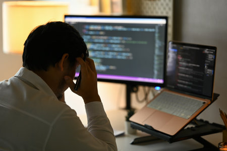 Overworked male programmer feeling frustrated and tired while working on computer code at night.の写真素材