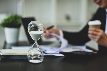 Closeup hourglass on office desk with blurred businessman working on background.