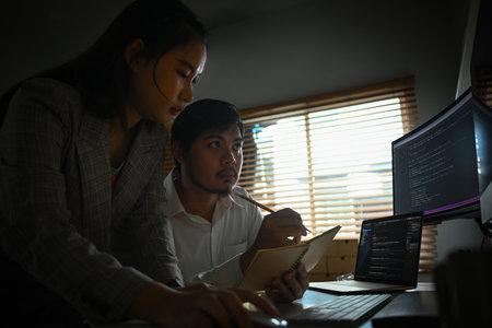 Team of young professionals brainstorming and working in software development in dark office.