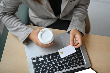 Above view of woman holding credit card and using laptop making payment or ordering via the...