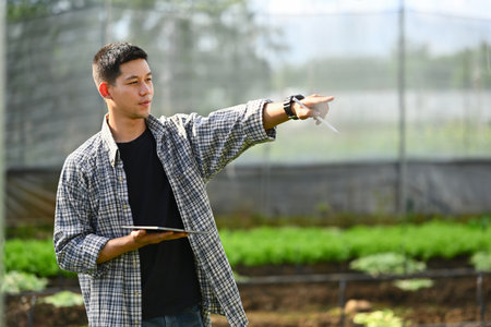 Farmer checking organic vegetable and recording farming data on digital tablet. Innovation and smart...
