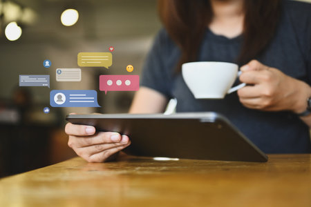 Young woman drinking coffee and using digital tablet with notification icons of like, message and...