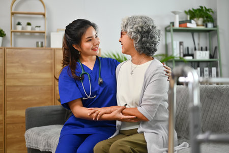 Caring general practitioner woman embracing shoulders of smiling 70s retired patient during home visit.の写真素材