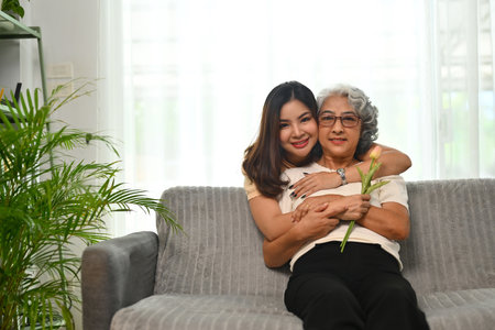 Affectionate young Asian woman hugging senior mother from back. International hug day concept.の写真素材