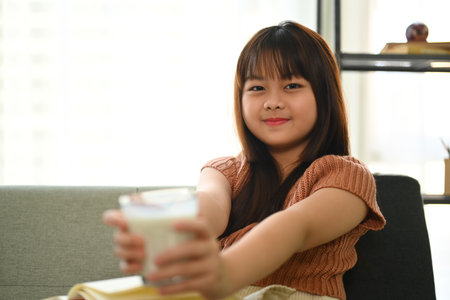 Cheerful Asian girl drinking milk for a breakfast in living roomの写真素材
