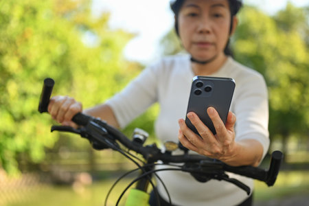 Senior woman hand using mobile phone checking route map location while riding exercise bicycleの写真素材