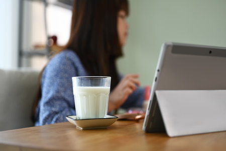 A glass and bottle of milk on wooden table with child girl doing homework on background.の写真素材