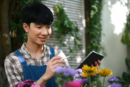 Portrait of happy Asian male florist in apron using digital tablet at small business flower shopの写真素材